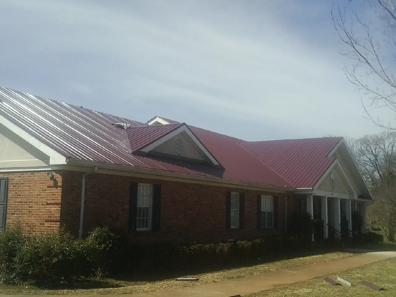 Red metal roof with gabled entries on a long brick building, from a Hail Damage Roof Repair job in Sonoma